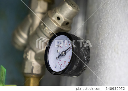 Industrial pressure gauge mounted on a metal plumbing valve indicates system load, representing technical maintenance, precision monitoring, and mechanical infrastructure control 140939952