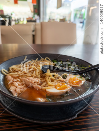 Steaming bowl of ramen with sliced chicken breast, marinated soft boiled egg and fresh seaweed resting on a wooden restaurant table, embodying authentic japanese culinary dining Steaming bowl of ramen with sliced chicken breast, marinated soft boiled egg and fresh seaweed resting on a wooden restaurant table, embodying authentic japanese culinary dining 140939957