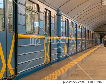 Blue subway train with yellow stripes docked at a modern underground station platform, representing urban public transport infrastructure, efficient city commuting, and daily travel Blue subway train with yellow stripes docked at a modern underground station platform, representing urban public transport infrastructure, efficient city commuting, and daily travel 140939960