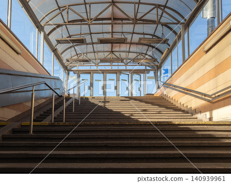 Concrete staircase leading up to an enclosed pedestrian walkway with glass walls and metal roof structure, reflecting urban architecture and public transportation transit connection Concrete staircase leading up to an enclosed pedestrian walkway with glass walls and metal roof structure, reflecting urban architecture and public transportation transit connection 140939961