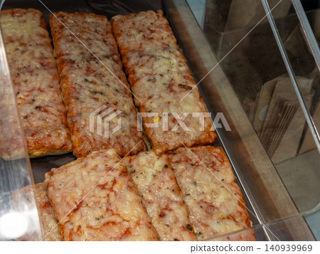 Fresh pizza slices with melted cheese and tomato sauce arranged in a commercial display case to highlight tempting bakery snacks for hungry customers in a casual fast food setting Fresh pizza slices with melted cheese and tomato sauce arranged in a commercial display case to highlight tempting bakery snacks for hungry customers in a casual fast food setting 140939969