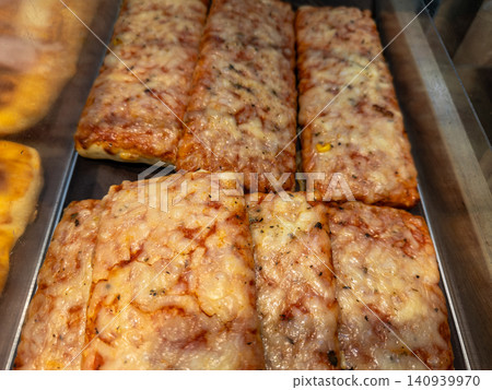 Freshly baked rectangular pizzas with melted mozzarella cheese and tomato sauce arranged in a retail display case for convenient fast food dining at a local bakery or cafe outlet Freshly baked rectangular pizzas with melted mozzarella cheese and tomato sauce arranged in a retail display case for convenient fast food dining at a local bakery or cafe outlet 140939970