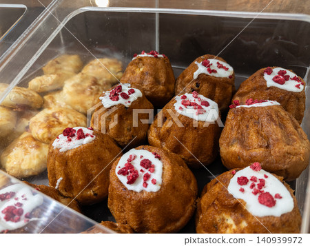 Freshly baked rum babas with white glaze and dried raspberry sprinkles inside a clear display case, perfect for a cozy morning breakfast bakery shop theme or gourmet snack display Freshly baked rum babas with white glaze and dried raspberry sprinkles inside a clear display case, perfect for a cozy morning breakfast bakery shop theme or gourmet snack display 140939972