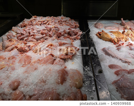 Raw chicken parts are displayed on crushed ice inside a modern supermarket refrigerated counter, providing a fresh selection for grocery shopping, meal prep, and culinary cooking Raw chicken parts are displayed on crushed ice inside a modern supermarket refrigerated counter, providing a fresh selection for grocery shopping, meal prep, and culinary cooking 140939988