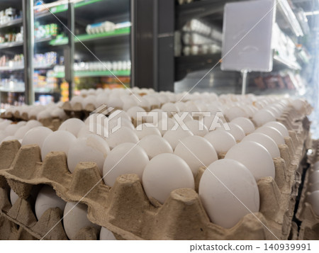 Fresh white chicken eggs are neatly arranged in cardboard cartons on a refrigerated supermarket shelf, showcasing an organized retail display of healthy protein food products today Fresh white chicken eggs are neatly arranged in cardboard cartons on a refrigerated supermarket shelf, showcasing an organized retail display of healthy protein food products today 140939991