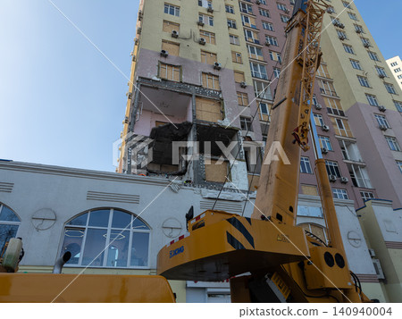 Yellow industrial crane parked near a damaged residential apartment building facade during urban restoration, depicting post-disaster recovery or structural reconstruction efforts Yellow industrial crane parked near a damaged residential apartment building facade during urban restoration, depicting post-disaster recovery or structural reconstruction efforts 140940004