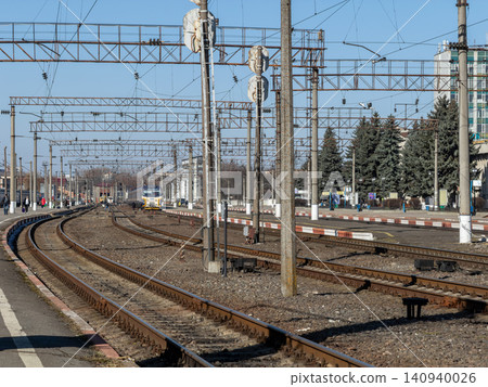A passenger train approaches the platform along metal tracks at a railway station, depicting public transport infrastructure under a clear sky for urban commute and travel concepts 140940026