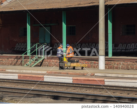 Railway workers in high visibility vests cleaning the platform at a train station, maintaining public infrastructure and ensuring safe transport environments for local daily commuters 140940028