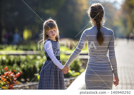 Moody cute child girl holding mother hand looking back on warm day outdoors. Family relationship and recreation. 140940292