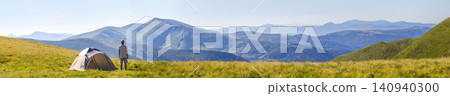 Hiker man standing near camping tent in carpathian mountains. Tourist enjoy mountain view. Travel concept. Hiker man standing near camping tent in carpathian mountains. Tourist enjoy mountain view. Travel concept. 140940300