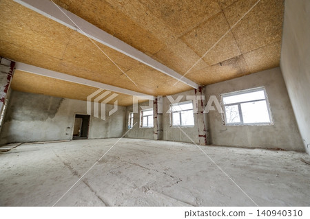 Unfinished apartment or house big loft room under reconstruction. Plywood ceiling, plastered walls, window openings, cement floor. Construction and renovation concept. Unfinished apartment or house big loft room under reconstruction. Plywood ceiling, plastered walls, window openings, cement floor. Construction and renovation concept. 140940310