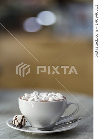 Mug of coffee with marshmallows on porcelain plate on blurred colorful interior bokeh background. Mug of coffee with marshmallows on porcelain plate on blurred colorful interior bokeh background. 140940313