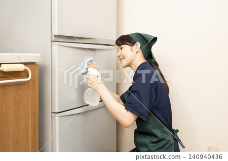 A female house cleaner wipes down a refrigerator. 140940436