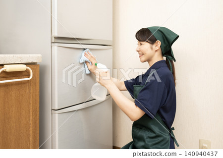 A female house cleaner wipes down a refrigerator. A female house cleaner wipes down a refrigerator. 140940437