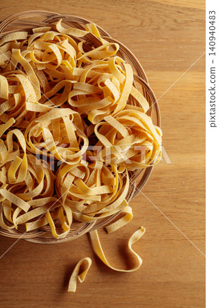 Raw dry pasta fettuccine in wicker dish on a wooden table. Raw dry pasta fettuccine in wicker dish on a wooden table. 140940483