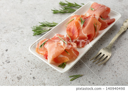Prosciutto slices with rosemary on a stone table. Prosciutto slices with rosemary on a stone table. 140940498