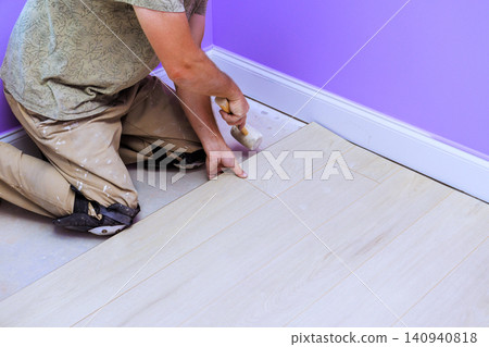 Diy worker kneels on laminate floor carefully places wooden plank while renovating room in house. Diy worker kneels on laminate floor carefully places wooden plank while renovating room in house. 140940818