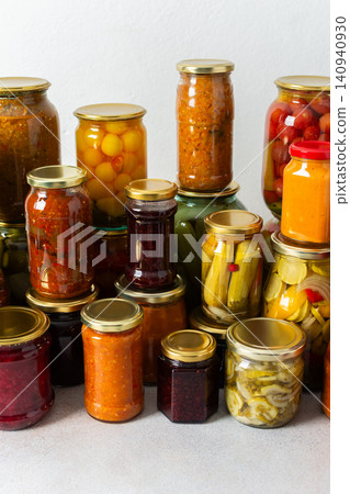 Canned vegetables and fruits are stacked on a shelf, prepared for winter use. Various jars hold different preserves, showcasing careful efforts for storing food during the season 140940930