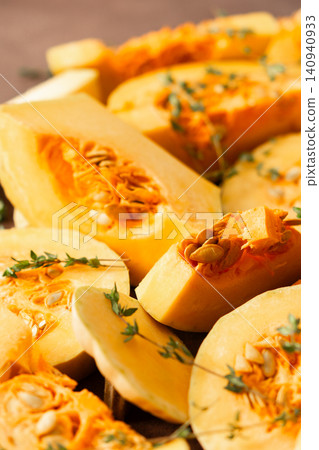 Slices of yellow squash are laid out on a wooden surface. Fresh thyme sprigs are placed on the squash. This scene shows preparation for cooking a meal or dish Slices of yellow squash are laid out on a wooden surface. Fresh thyme sprigs are placed on the squash. This scene shows preparation for cooking a meal or dish 140940933