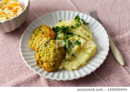 This plate features mashed potatoes, two turkey meatballs, and a side of fermented cabbage. Fresh herbs are sprinkled on top, creating a balanced meal choice This plate features mashed potatoes, two turkey meatballs, and a side of fermented cabbage. Fresh herbs are sprinkled on top, creating a balanced meal choice 140940944