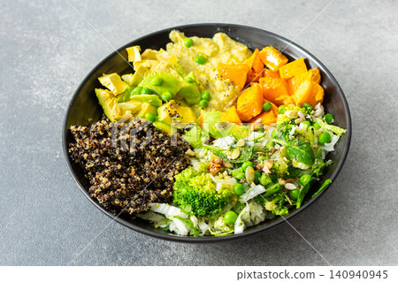 A quinoa bowl is arranged with roasted pumpkin, hummus, and a fresh salad. Plates are set on a table with utensils. Sunshine comes through the window A quinoa bowl is arranged with roasted pumpkin, hummus, and a fresh salad. Plates are set on a table with utensils. Sunshine comes through the window 140940945