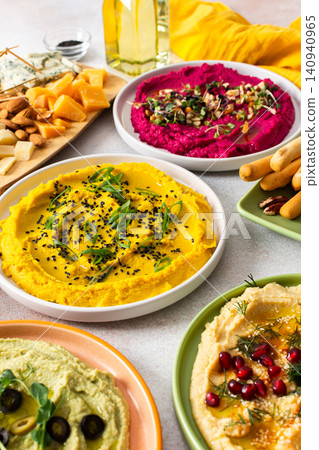 A variety of hummus flavors including turmeric, classic, and broccoli are served with fresh bread, nuts, and garnishes on a colorful charcuterie board, perfect for sharing A variety of hummus flavors including turmeric, classic, and broccoli are served with fresh bread, nuts, and garnishes on a colorful charcuterie board, perfect for sharing 140940965