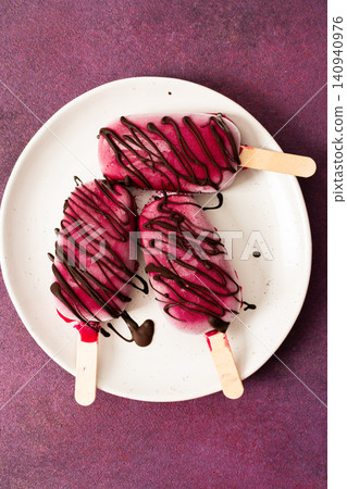 Three popsicles made from strawberries, bananas, beets, and Greek yogurt sit on a plate. They are drizzled with chocolate and enjoyed during a sunny day with friends Three popsicles made from strawberries, bananas, beets, and Greek yogurt sit on a plate. They are drizzled with chocolate and enjoyed during a sunny day with friends 140940976