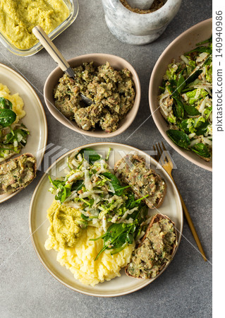 Boiled potatoes are served with hummus alongside a gluten free sandwich filled with herring mince and fresh salad on a simple plate during breakfast time 140940986