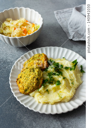 This plate features mashed potatoes, two turkey meatballs, and a side of fermented cabbage. Fresh herbs are sprinkled on top, creating a balanced meal choice This plate features mashed potatoes, two turkey meatballs, and a side of fermented cabbage. Fresh herbs are sprinkled on top, creating a balanced meal choice 140941030
