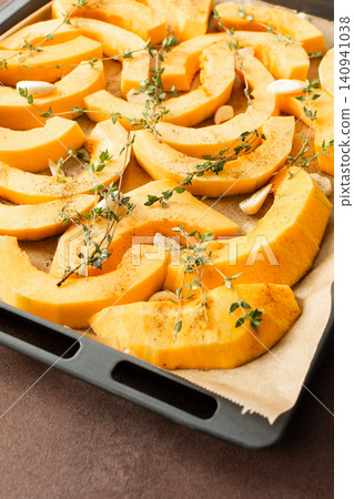 Butternut squash slices are arranged on a tray with herbs and garlic, ready for roasting. This is part of a cooking process in a kitchen setting Butternut squash slices are arranged on a tray with herbs and garlic, ready for roasting. This is part of a cooking process in a kitchen setting 140941038