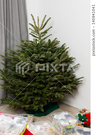 People set up a Christmas tree in their home with various boxes of holiday ornaments nearby. The area shows items ready to be used for decorating the tree. It is winter time People set up a Christmas tree in their home with various boxes of holiday ornaments nearby. The area shows items ready to be used for decorating the tree. It is winter time 140941041