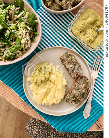 A plate shows a serving of boiled potatoes with hummus, a gluten free bread sandwich filled with herring mince, and fresh salad. This breakfast offers a nutritious start to the day A plate shows a serving of boiled potatoes with hummus, a gluten free bread sandwich filled with herring mince, and fresh salad. This breakfast offers a nutritious start to the day 140941797