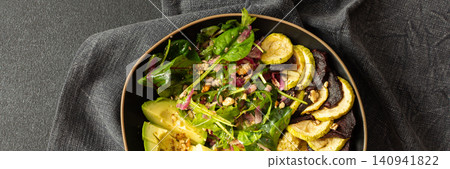 A bowl contains millet porridge next to baked zucchini and beets. There is a salad made of spinach, arugula, and pink radish with nuts and seeds. The setting is simple and clean, banner A bowl contains millet porridge next to baked zucchini and beets. There is a salad made of spinach, arugula, and pink radish with nuts and seeds. The setting is simple and clean, banner 140941822
