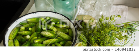 Cucumbers are being cleaned and sorted in a kitchen while glass jars are ready for canning. Ingredients are organized for preserving during the winter months ahead, banner 140941832