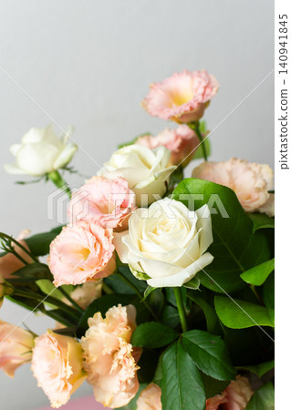 Fresh roses and eustomas are arranged in a bouquet with green leaves. The setting has a plain background and bright lighting. This moment captures floral beauty 140941845