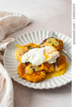 A plate of millet pancakes topped with hollandaise sauce and a poached egg sits on a table. This dish is offered as a healthy option for breakfast or lunch 140941855