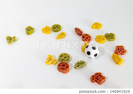 Soccer themed pasta shapes with a small soccer ball scattered on a white surface, creating playful football inspired food art. 140941929