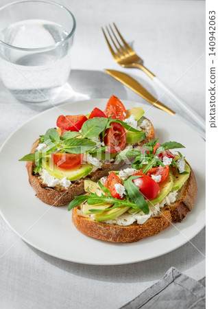 Two toasts with avocado, cream cheese, feta, tomato and arugula on a concrete background Two toasts with avocado, cream cheese, feta, tomato and arugula on a concrete background 140942063