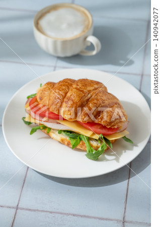 A golden croissant sandwich with ham, cheese, tomato, and arugula on a tile background A golden croissant sandwich with ham, cheese, tomato, and arugula on a tile background 140942077