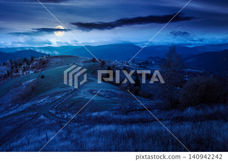 winding rural dirt path through hill at night. rolling countryside of ukraine in fall color. cloudy sky in full moon light. carpathian mountains in autumn winding rural dirt path through hill at night. rolling countryside of ukraine in fall color. cloudy sky in full moon light. carpathian mountains in autumn 140942242