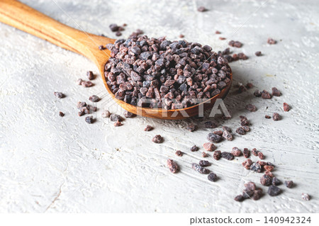 Crystals of black salt, on a wooden spoon, on a light surface, top view, Crystals of black salt, on a wooden spoon, on a light surface, top view, 140942324