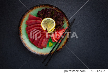 Fresh tuna sashimi served with lemon, wasabi, and pickled ginger on a dark background 140942334