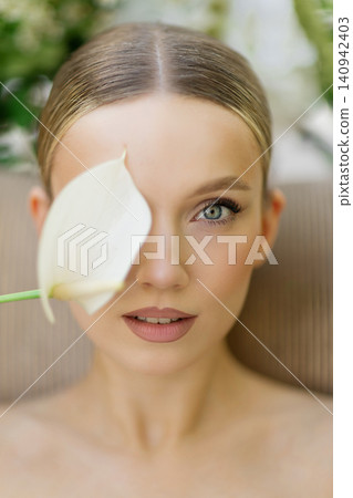 Woman with fresh skin holding calla lily on face Woman with fresh skin holding calla lily on face 140942403