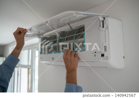 Man's hands open wall-mounted air conditioner to remove dusty filter, cooling system maintenance. Man's hands open wall-mounted air conditioner to remove dusty filter, cooling system maintenance. 140942567