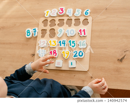 boy learns to count by laying out numbers from 1 to 20 on the board, boy 4-5 years old European appearance, at home in the living room sitting at the table, preparation for school. High quality photo boy learns to count by laying out numbers from 1 to 20 on the board, boy 4-5 years old European appearance, at home in the living room sitting at the table, preparation for school. High quality photo 140942574