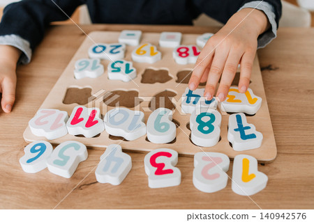 boy learns to count by laying out numbers from 1 to 20 on the board, boy 4-5 years old European appearance, at home in the living room sitting at the table, preparation for school. High quality photo boy learns to count by laying out numbers from 1 to 20 on the board, boy 4-5 years old European appearance, at home in the living room sitting at the table, preparation for school. High quality photo 140942576