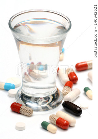 Scattered Pills Around a Glass of Brandy on a White Background Scattered Pills Around a Glass of Brandy on a White Background 140942621
