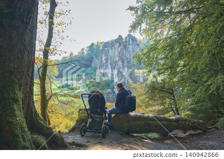 dad sits on a fallen tree trunk next to a baby in a stroller with his back to the camera dad sits on a fallen tree trunk next to a baby in a stroller with his back to the camera 140942866