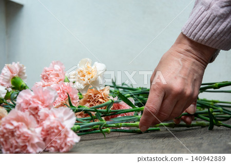 A hand touches and adjusts pink and white flowers on a wooden table. This shows the process of arranging flowers indoors at daytime A hand touches and adjusts pink and white flowers on a wooden table. This shows the process of arranging flowers indoors at daytime 140942889