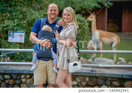 A young family in Moscow zoo with a one-year-old baby, in the background a llama looks at the camera on a warm summer day. High quality photo A young family in Moscow zoo with a one-year-old baby, in the background a llama looks at the camera on a warm summer day. High quality photo 140942941